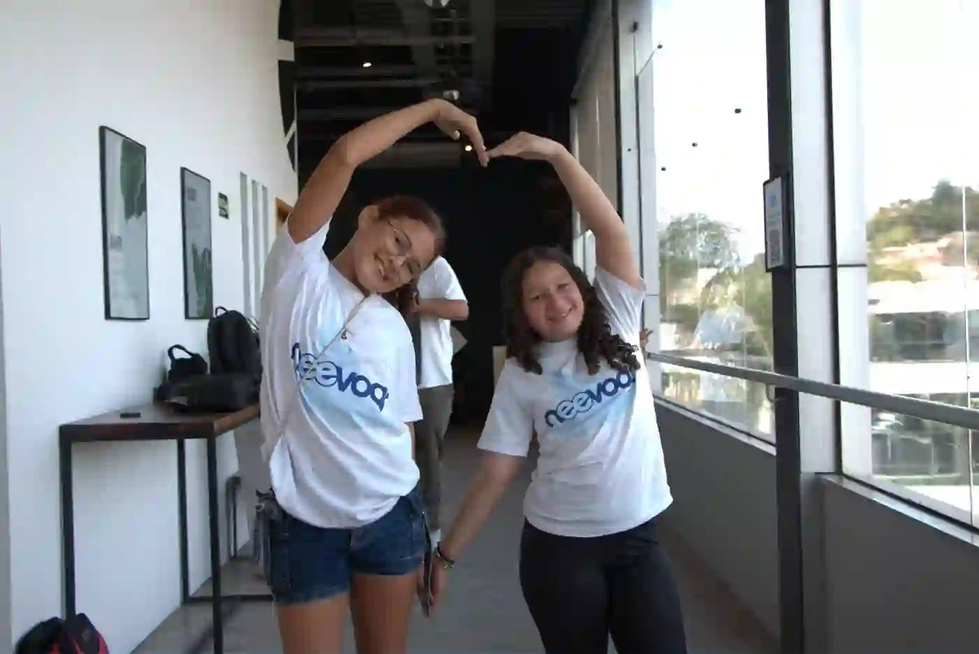 Duas meninas do Instituto Neevoar sorrindo e fazendo coração com as mãos